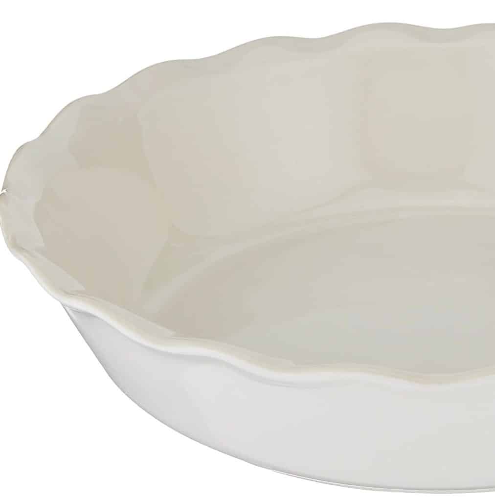 A white ceramic pie dish with a scalloped edge, shown from a side angle, awaits fall pies and cakes. The dish's glossy finish enhances its smooth texture and elegant design, making it the perfect backdrop for seasonal delights.